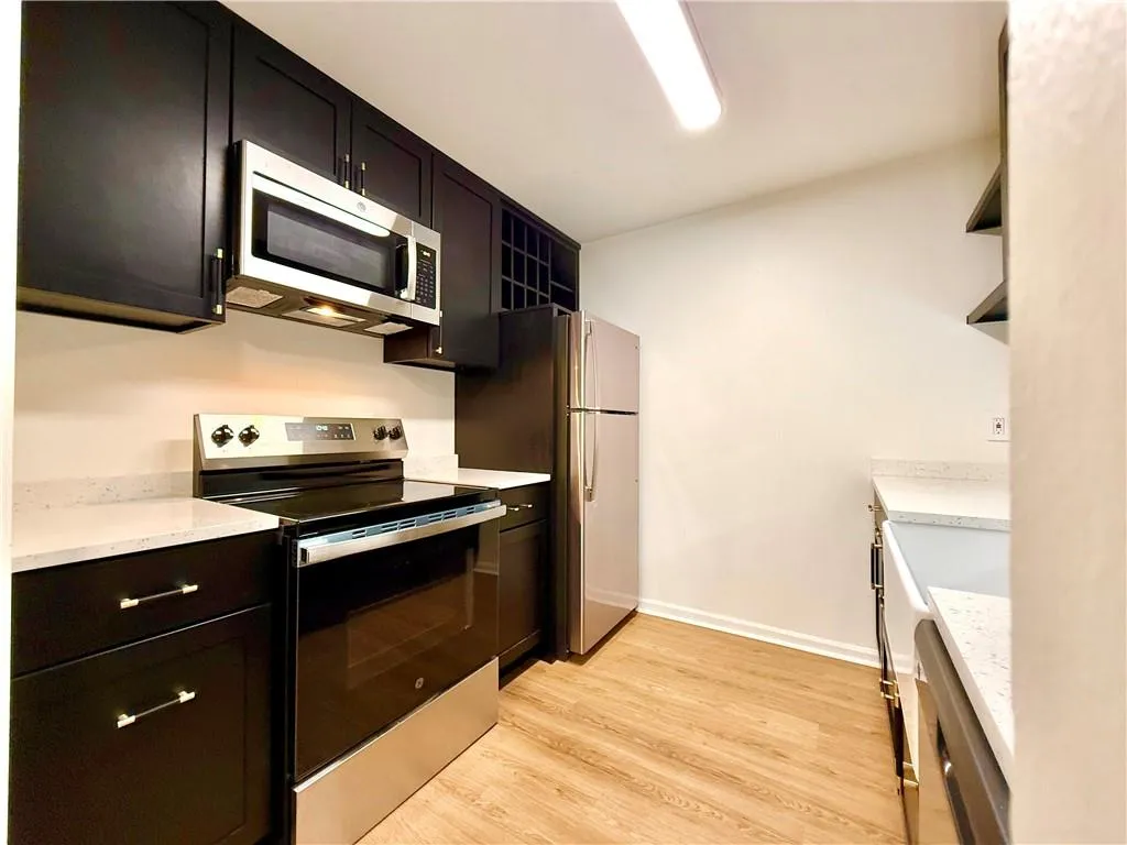 Kitchen featuring stainless steel appliances, open shelves, light wood-style floors, and light stone countertops
