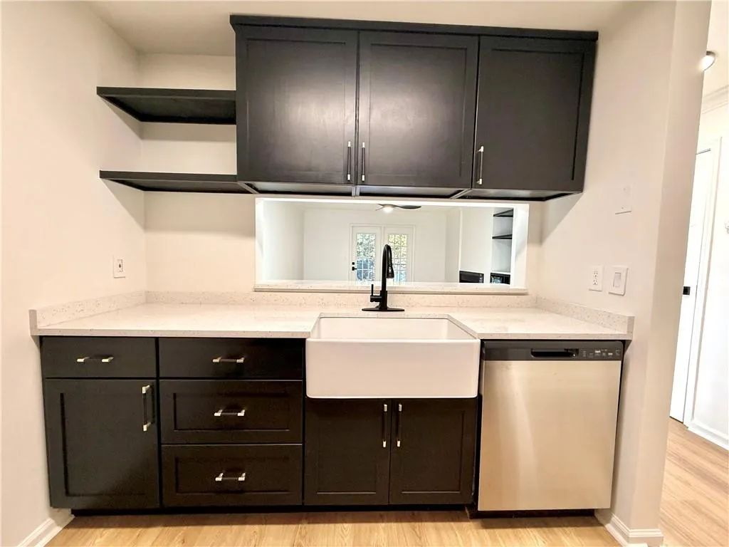 Kitchen featuring open shelves, stainless steel dishwasher, dark cabinets, light stone countertops, and light wood finished floors