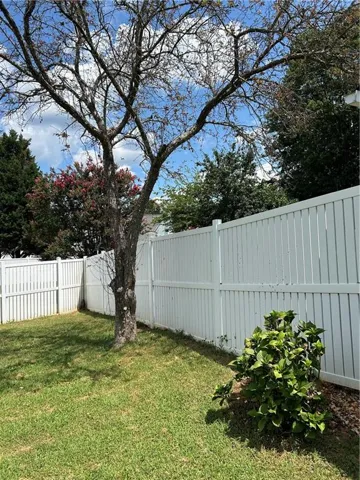 Enclosed backyard with a white privacy fence, green lawn, and mature trees
