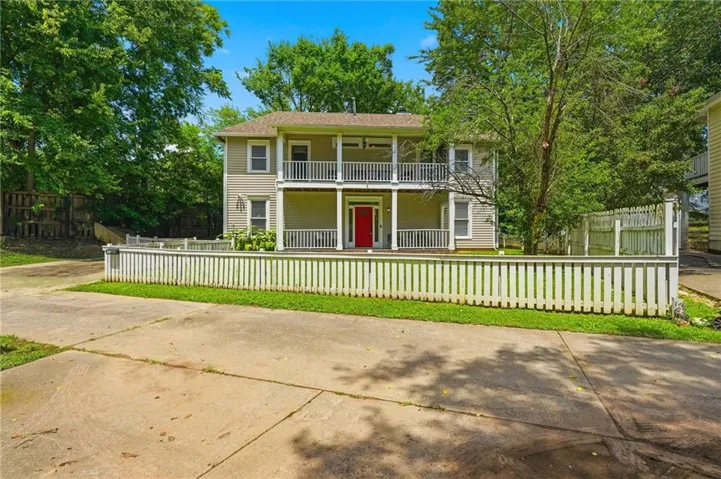Two-story residence featuring light-colored siding, a red front door, and a white picket fence