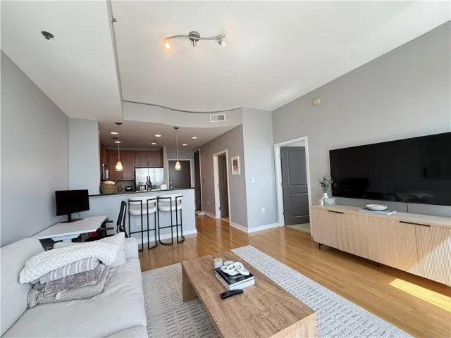 Open-concept living space featuring wood-finish flooring and a kitchen with dark cabinetry, stainless steel appliances, and pendant lighting
