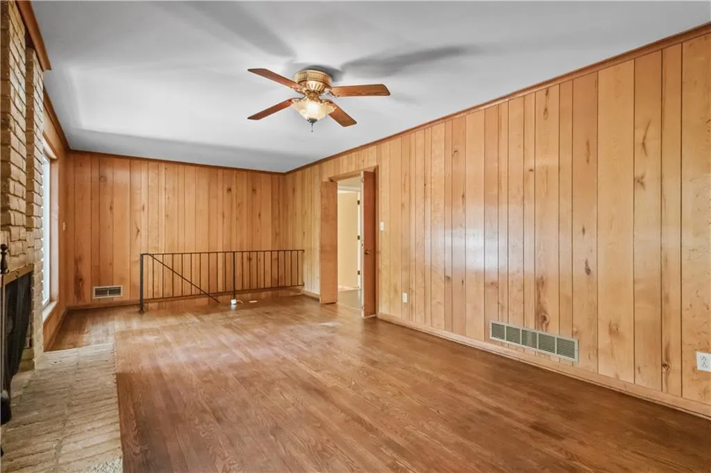 Spare room featuring wood-type flooring, wooden walls, a fireplace, and ceiling fan Spare room featuring wood-type flooring, wooden walls, a fireplace, and ceiling fan
