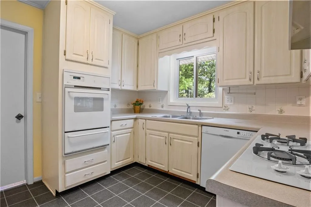 Kitchen with decorative backsplash, white appliances, sink, and dark tile patterned flooring Kitchen with decorative backsplash, white appliances, sink, and dark tile patterned flooring