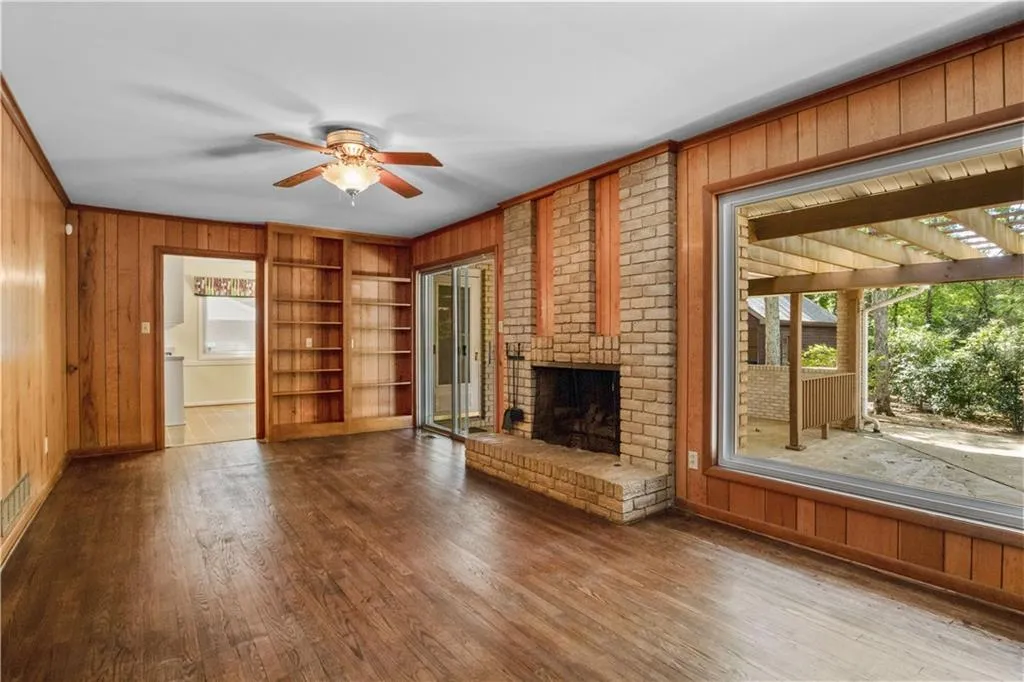 Unfurnished living room featuring wood-type flooring, ceiling fan, built in shelves, and a wealth of natural light Unfurnished living room featuring wood-type flooring, ceiling fan, built in shelves, and a wealth of natural light