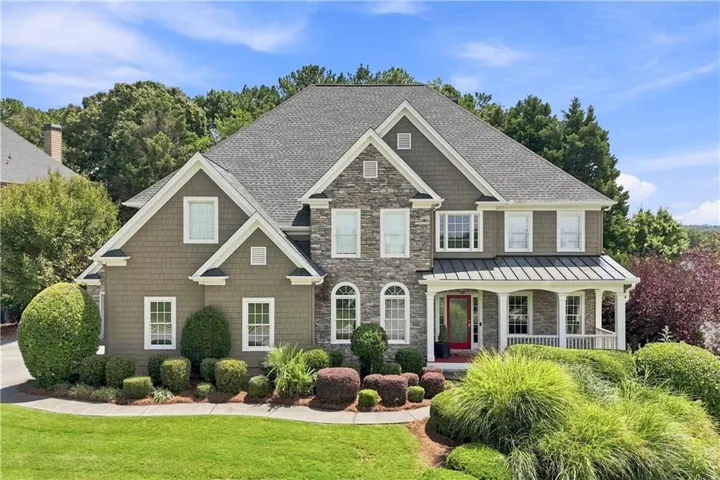 Multi-gable roofline, stone and shake siding exterior, covered porch with white columns, red front door, and mature landscaping
