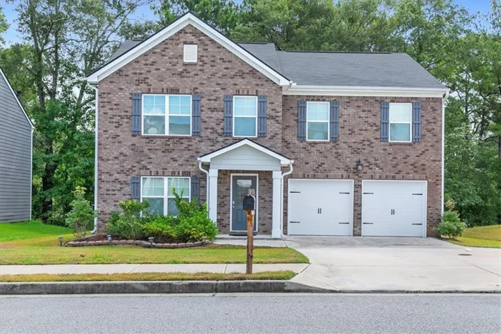 Traditional two-story residence featuring a brick facade, white trim, and a dark shingle roof