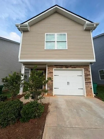 Exterior featuring siding, a stone facade, a single-car garage, and a concrete driveway