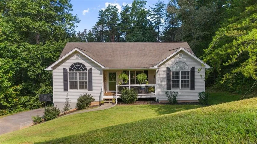 Gable-front home with light-colored siding, a covered porch, dark window shutters, and an arched transom window