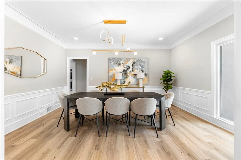 Dining room with a decorative wall, wainscoting, ornamental molding, and light wood-style floors