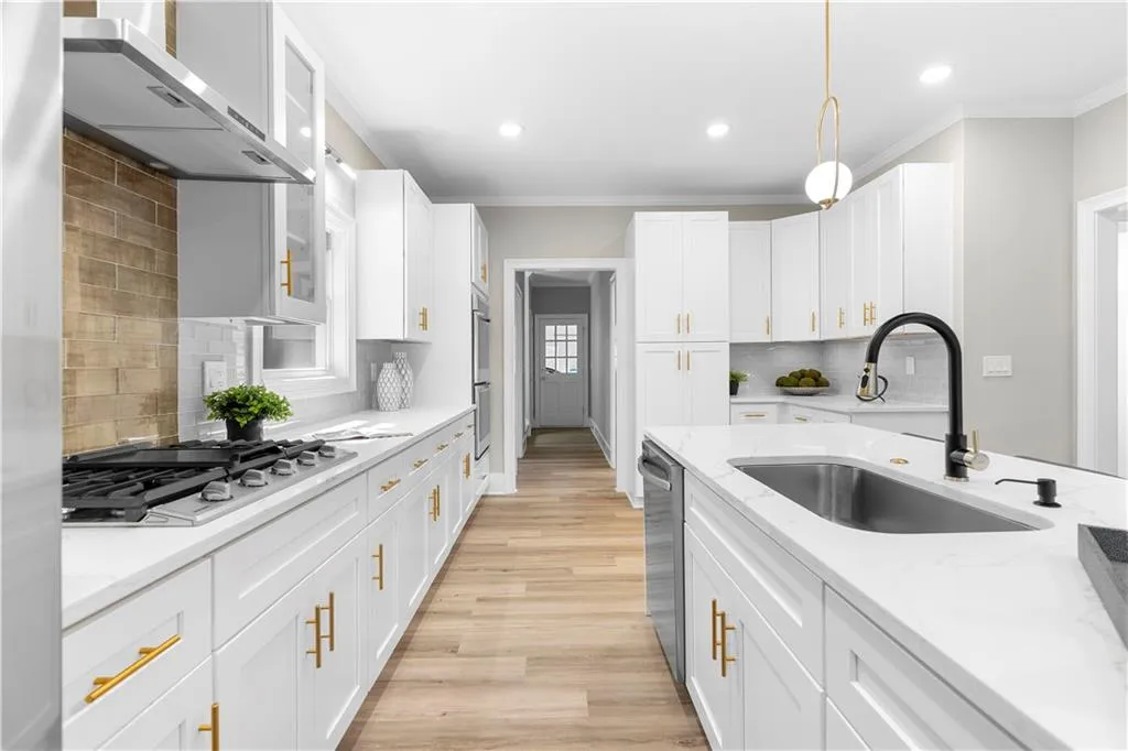 Kitchen with backsplash, wall chimney exhaust hood, light wood-style floors, white cabinetry, and ornamental molding