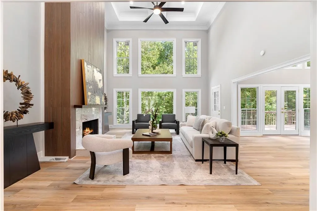 Living room featuring a premium fireplace, crown molding, light wood-style floors, a ceiling fan, and a high ceiling