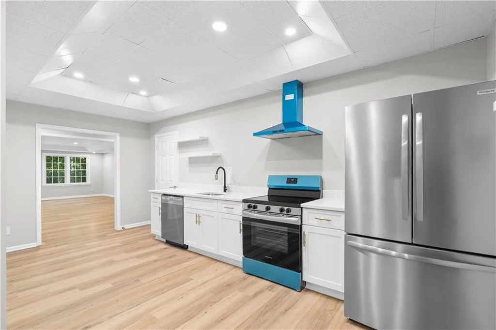 Kitchen featuring appliances with stainless steel finishes, light countertops, wall chimney exhaust hood, white cabinets, and a drop ceiling
