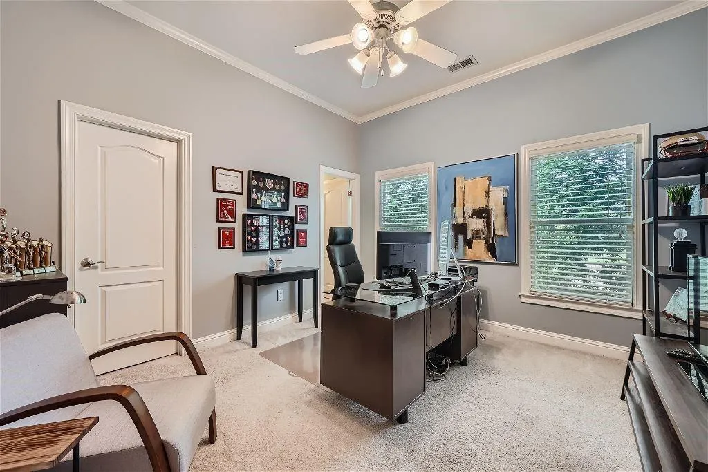 Carpeted office space with ceiling fan and crown molding