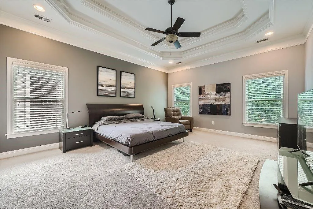 Carpeted bedroom with ceiling fan, ornamental molding, and a tray ceiling