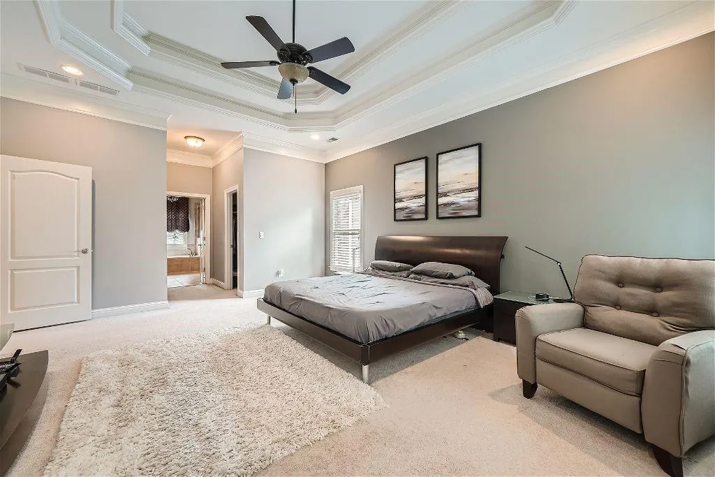 Carpeted bedroom featuring ceiling fan, a tray ceiling, crown molding, and connected bathroom