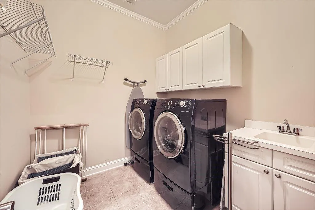 Laundry room with cabinets, ornamental molding, washing machine and clothes dryer, sink, and light tile flooring
