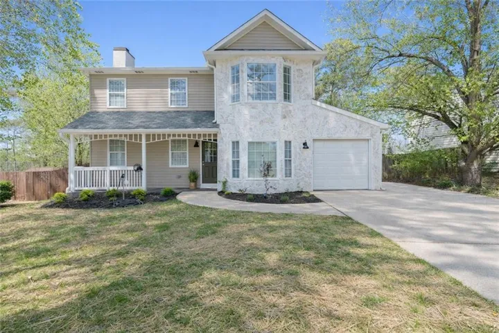 Two-story residence featuring a combination of stucco and siding, an attached garage, a covered front porch, and a paved driveway
