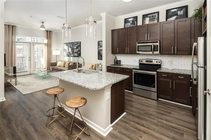 Kitchen featuring stainless steel appliances, ornamental molding, light stone countertops, dark brown cabinets, and a breakfast bar