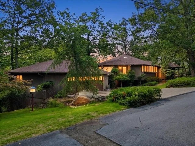 Circular modern residence with multiple large windows, a two-car garage, and mature tree landscaping