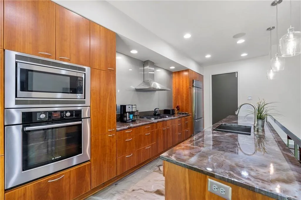 Kitchen with dark stone counters, brown cabinetry, built in appliances, modern cabinets, and pendant lighting