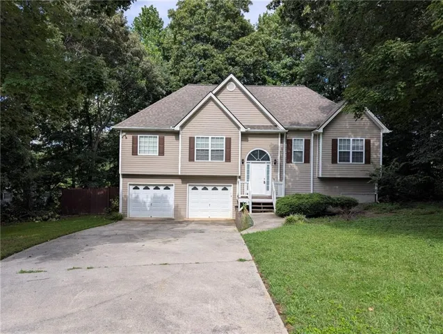 Split-level property featuring a two-car garage, front entry with arched transom window, and mature landscaping