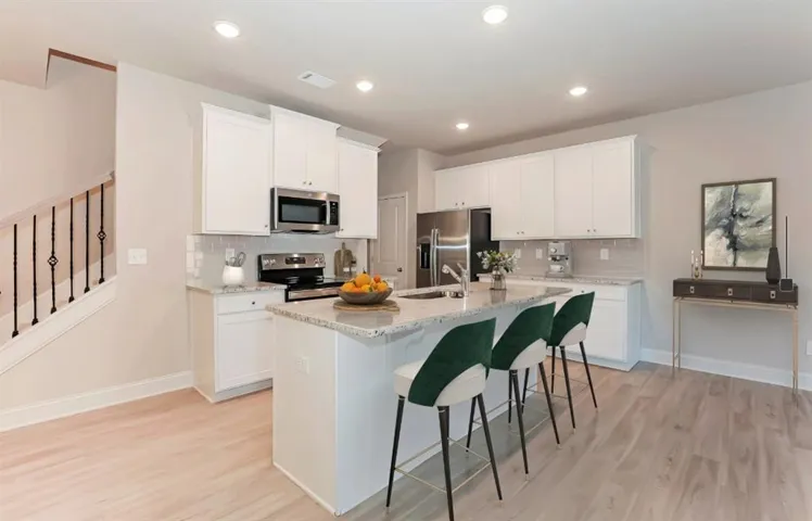 Kitchen featuring stainless steel appliances, light wood-style floors, light stone counters, white cabinets, and recessed lighting