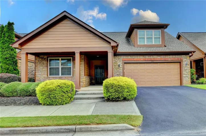 Welcoming brick and stone facade featuring a covered entry portico with substantial columns, multi-pane windows with dark trim, and a two-car garage with paneled door