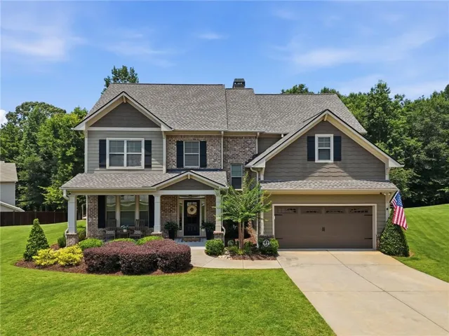 Multi-story residence featuring a combination of brick and siding, a covered front porch with white columns, a two-car garage, and a concrete driveway