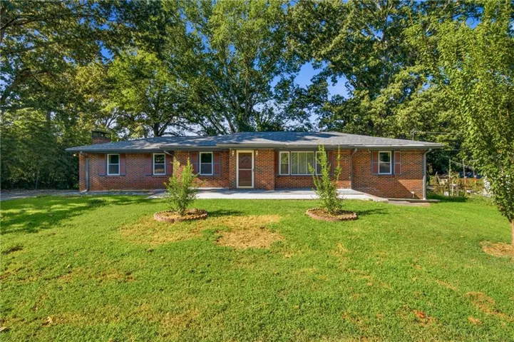 Brick exterior with a gray shingle roof, complemented by a front yard featuring mature trees and a manicured lawn