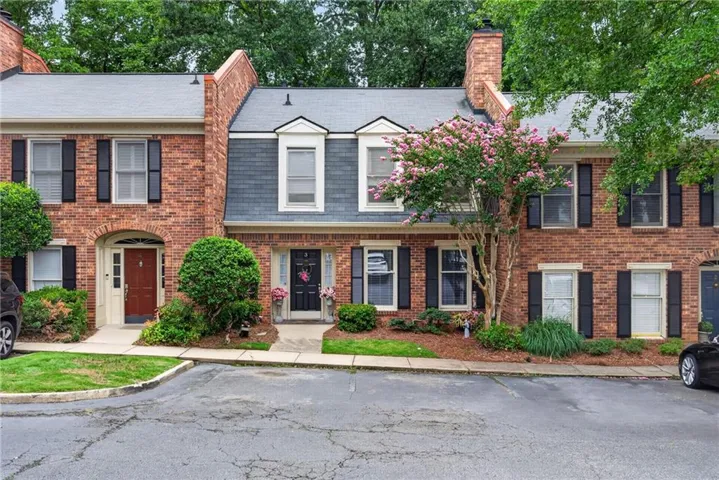 Brick exterior with a dormer window, black louvered shutters, and mature landscaping
