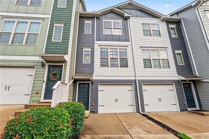 Multi-level townhome exterior featuring an attached garage, a driveway, and shrubbery