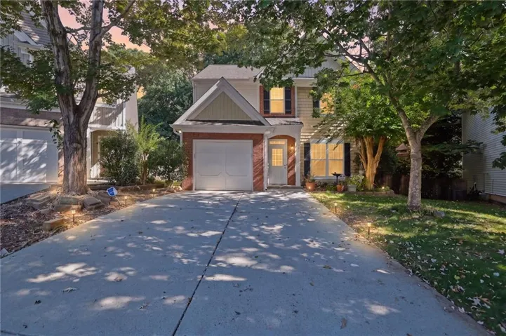 Two-story residence featuring a brick and siding facade, an attached garage, a paved driveway, and mature trees