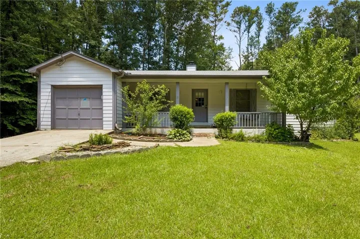 Single-story residence featuring a covered front porch, attached garage with driveway, and a front yard with established landscaping