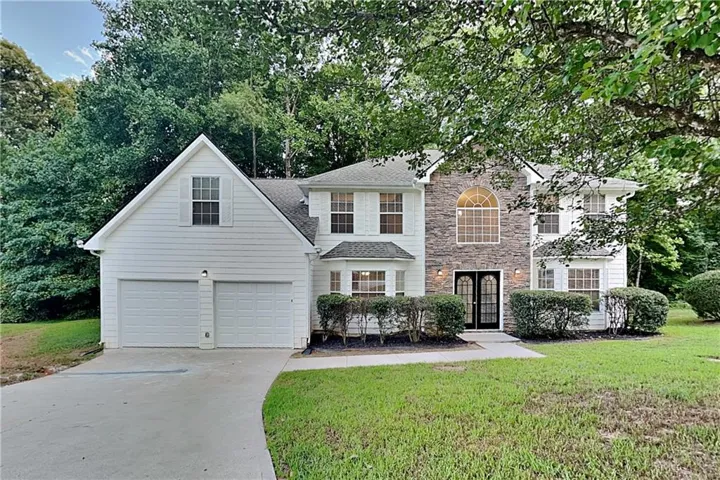 Two-story residence featuring white siding and stone accents, a two-car garage, and an arched window above double entry doors