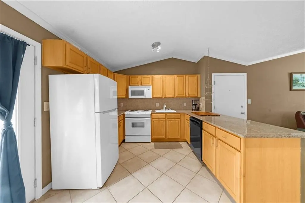 Kitchen featuring white appliances, a peninsula, lofted ceiling, light tile patterned floors, and crown molding