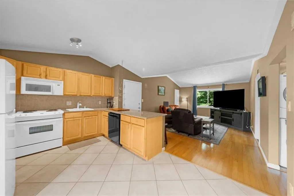 Kitchen with white appliances, light brown cabinets, open floor plan, lofted ceiling, and a peninsula