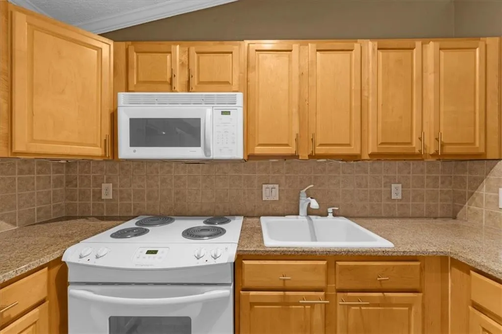 Kitchen with white appliances, tasteful backsplash, and lofted ceiling