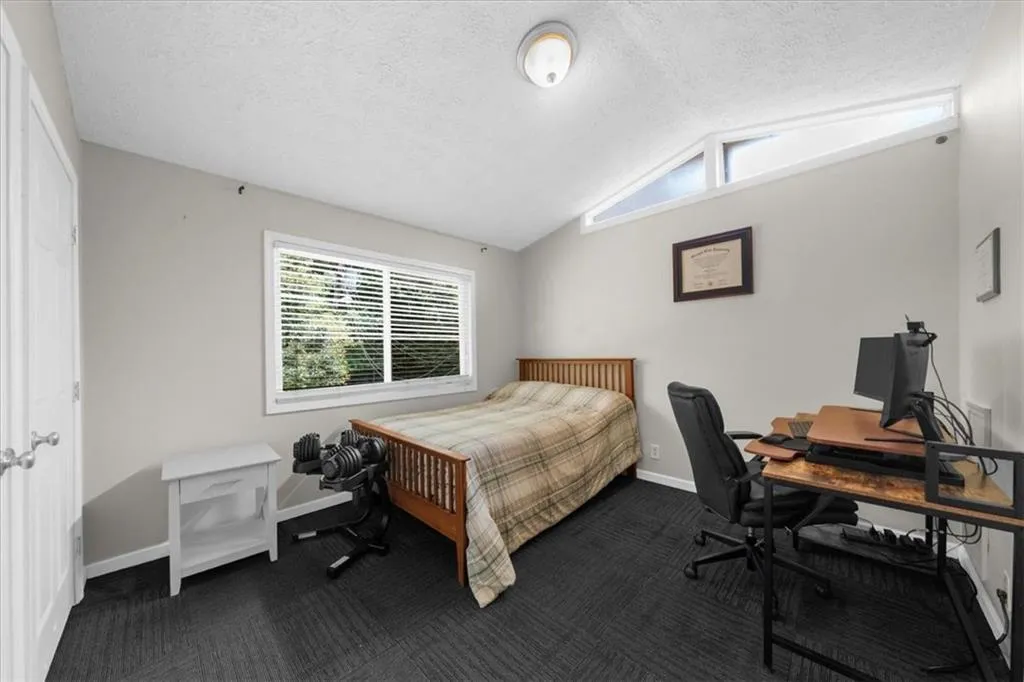 Bedroom with lofted ceiling, dark colored carpet, an office area, and a textured ceiling