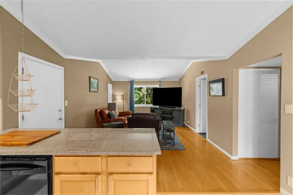 Kitchen featuring light wood-style flooring, ornamental molding, dishwasher, light brown cabinetry, and open floor plan