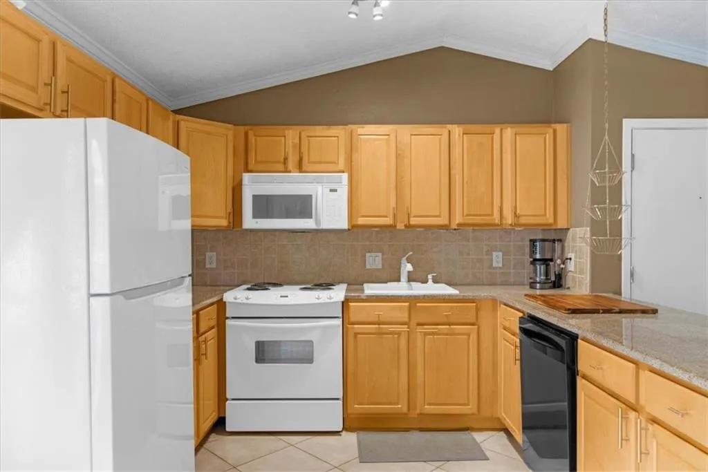 Kitchen with white appliances, lofted ceiling, tasteful backsplash, light brown cabinetry, and light tile patterned flooring