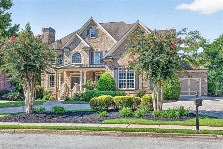 Brick and stone facade residence featuring a covered front porch, arched window detailing, an attached two-car garage, and established landscaping