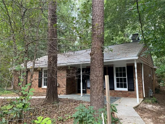 Brick-clad exterior featuring white window trim, black louvered shutters, an asphalt shingle roof, and a covered porch supported by white columns