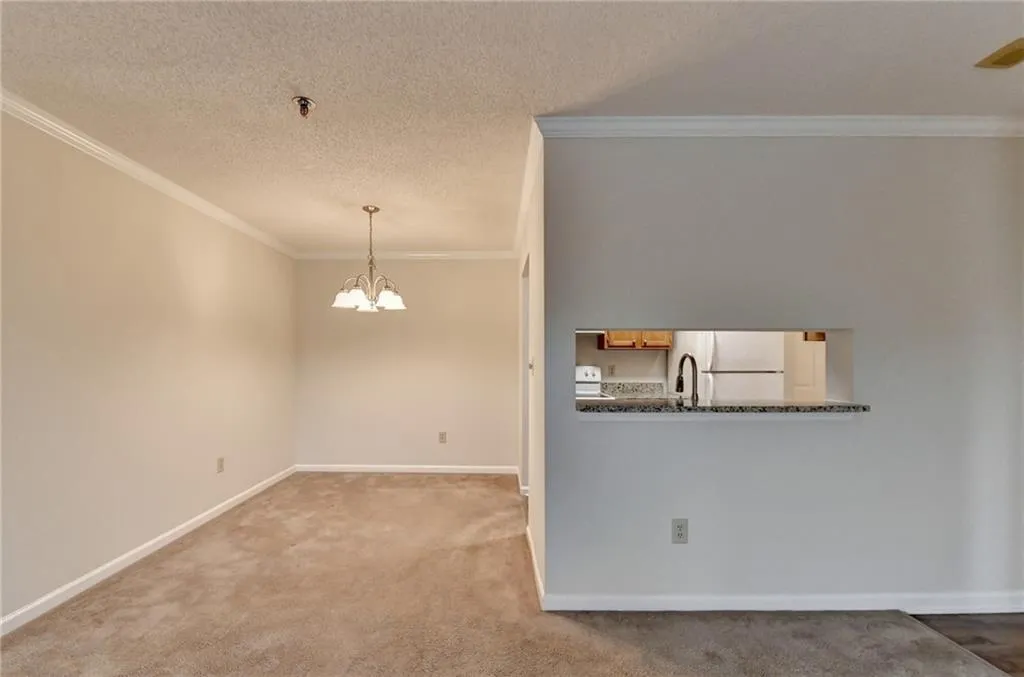 Empty room with an inviting chandelier, sink, ornamental molding, a textured ceiling, and light carpet