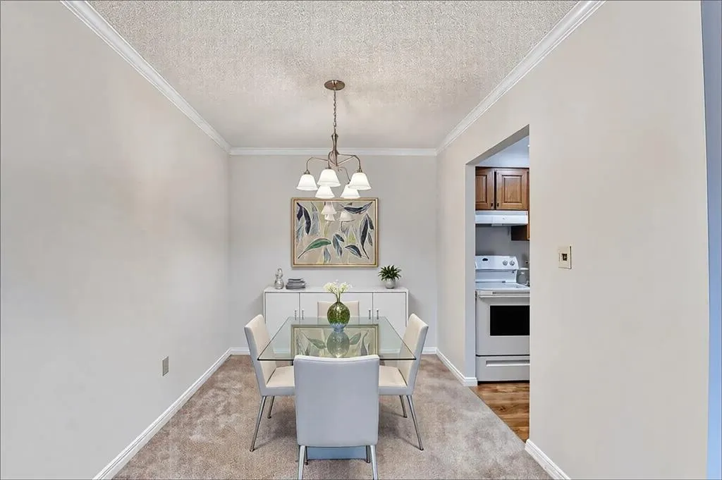 Carpeted dining area featuring a textured ceiling, ornamental molding, and a chandelier