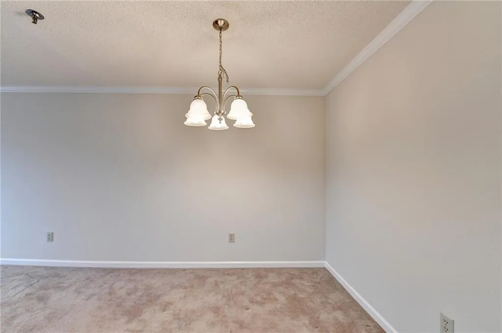 Carpeted empty room with crown molding, an inviting chandelier, and a textured ceiling