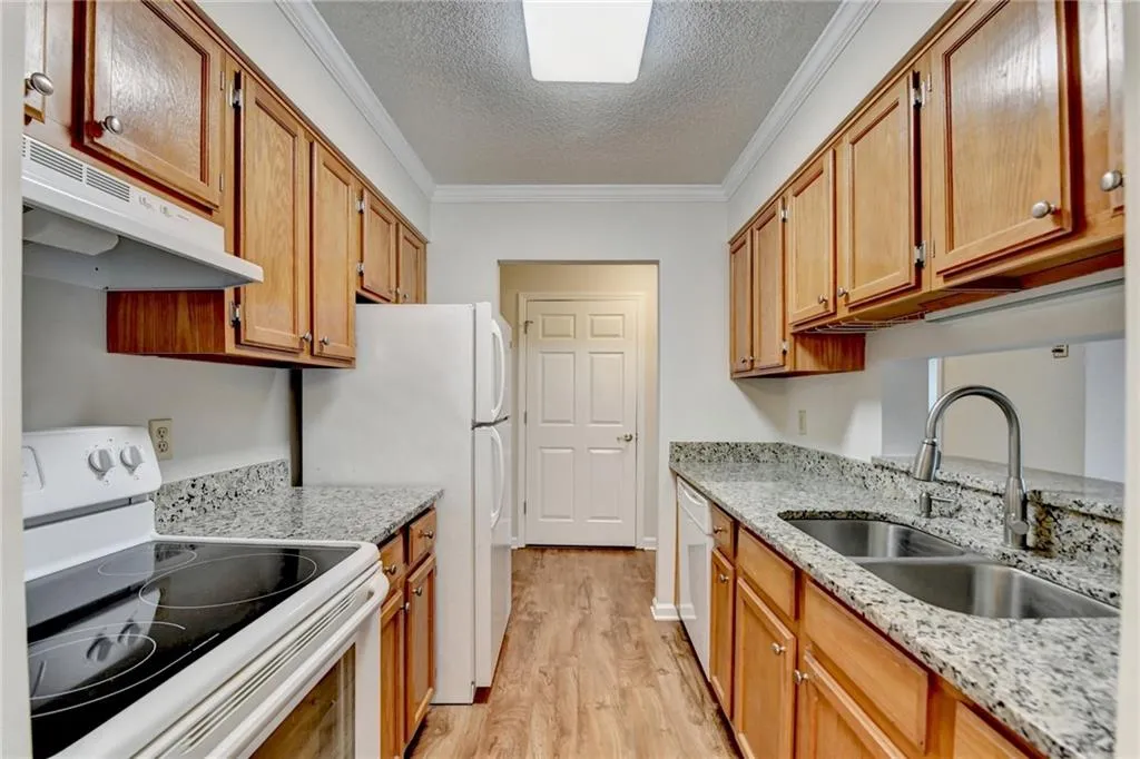 Kitchen featuring white appliances, light stone counters, light hardwood / wood-style floors, crown molding, and sink
