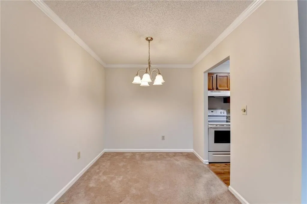 Unfurnished dining area featuring carpet floors, a chandelier, crown molding, and a textured ceiling