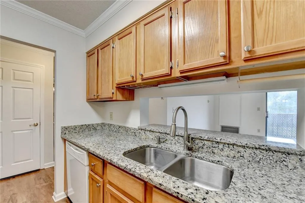 Kitchen with light hardwood / wood-style flooring, light stone countertops, crown molding, sink, and white dishwasher