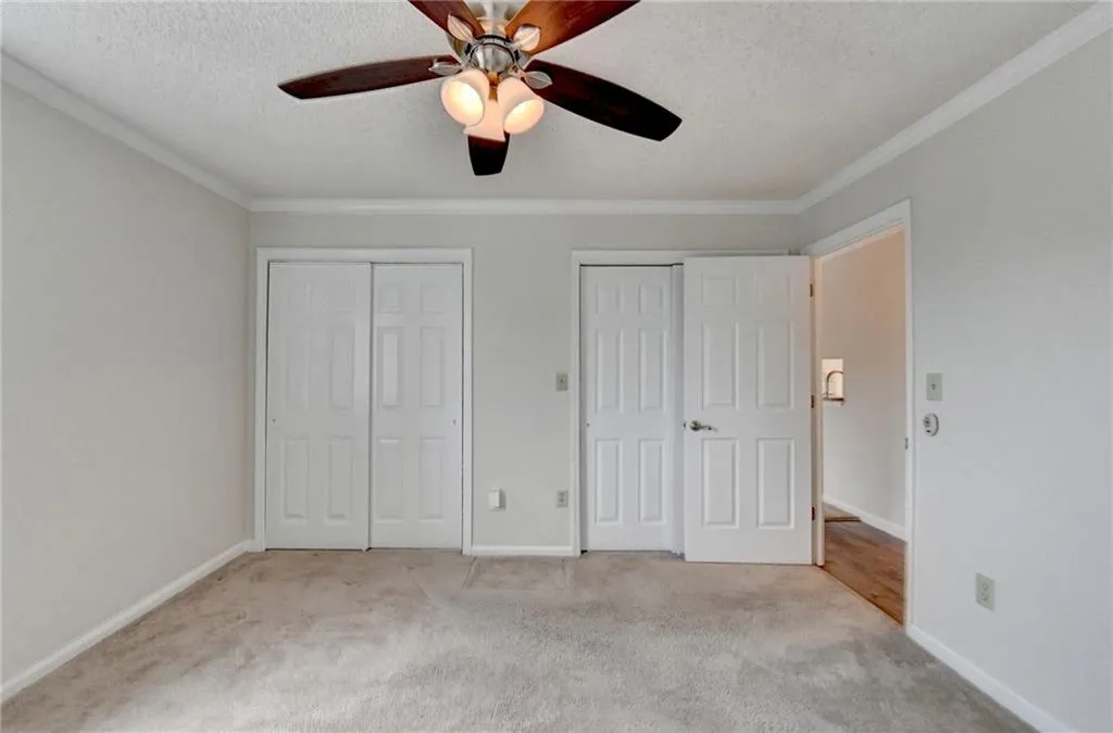 Unfurnished bedroom featuring light carpet, ornamental molding, a textured ceiling, and two closets