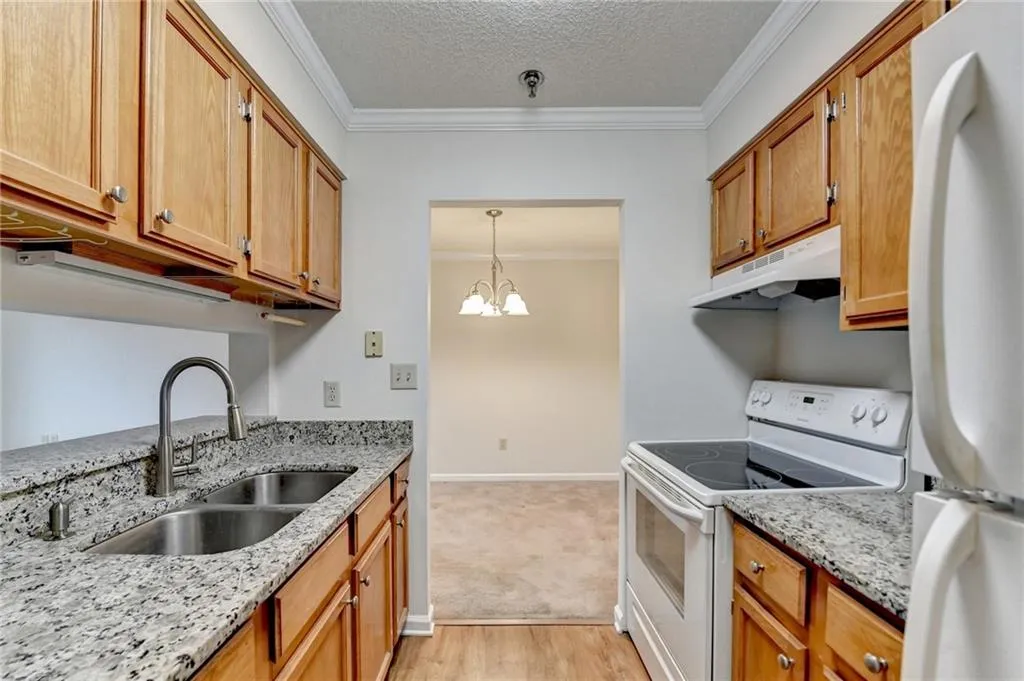 Kitchen featuring white appliances, sink, light stone counters, hanging light fixtures, and ornamental molding